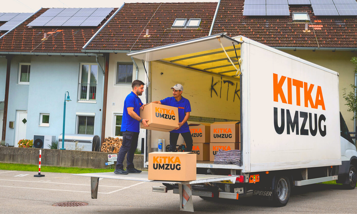 Offener Umzugswagen von KITKA vor einem Wohnhaus, zwei Helfer beladen ihn